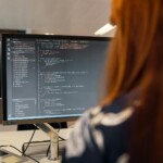 Ingénieur en informatique analysant du code sur plusieurs écrans dans un open space moderne