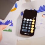 Personne consultant son compte bancaire sur smartphone près d'un carnet d'épargne