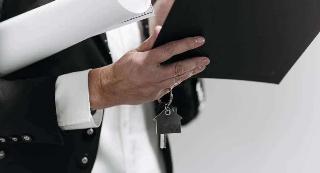 Main sur plan d’architecte avec contrats de vente immobilière, ambiance bureau d’affaires
