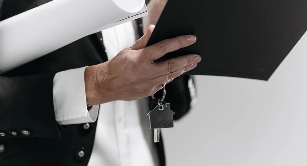 Main sur plan d’architecte avec contrats de vente immobilière, ambiance bureau d’affaires