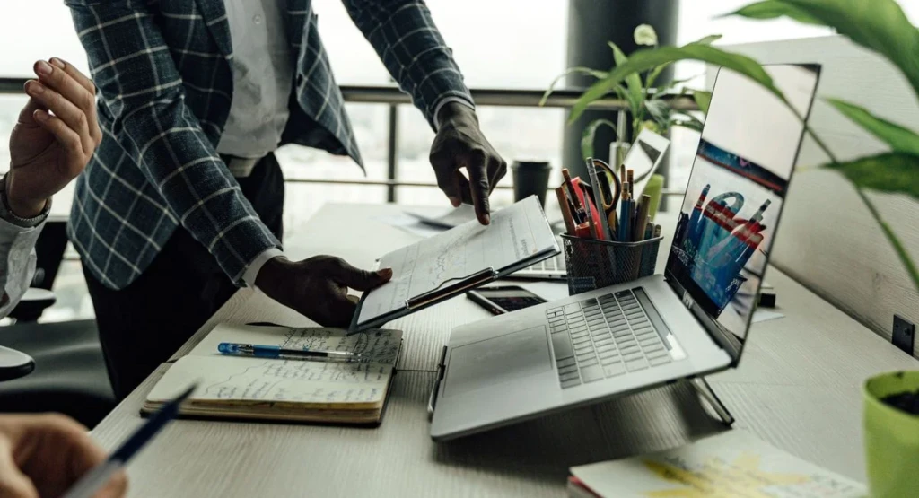 Scène de travail intense sur ordinateur portable, documents business visibles sur le bureau