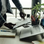 Scène de travail intense sur ordinateur portable, documents business visibles sur le bureau